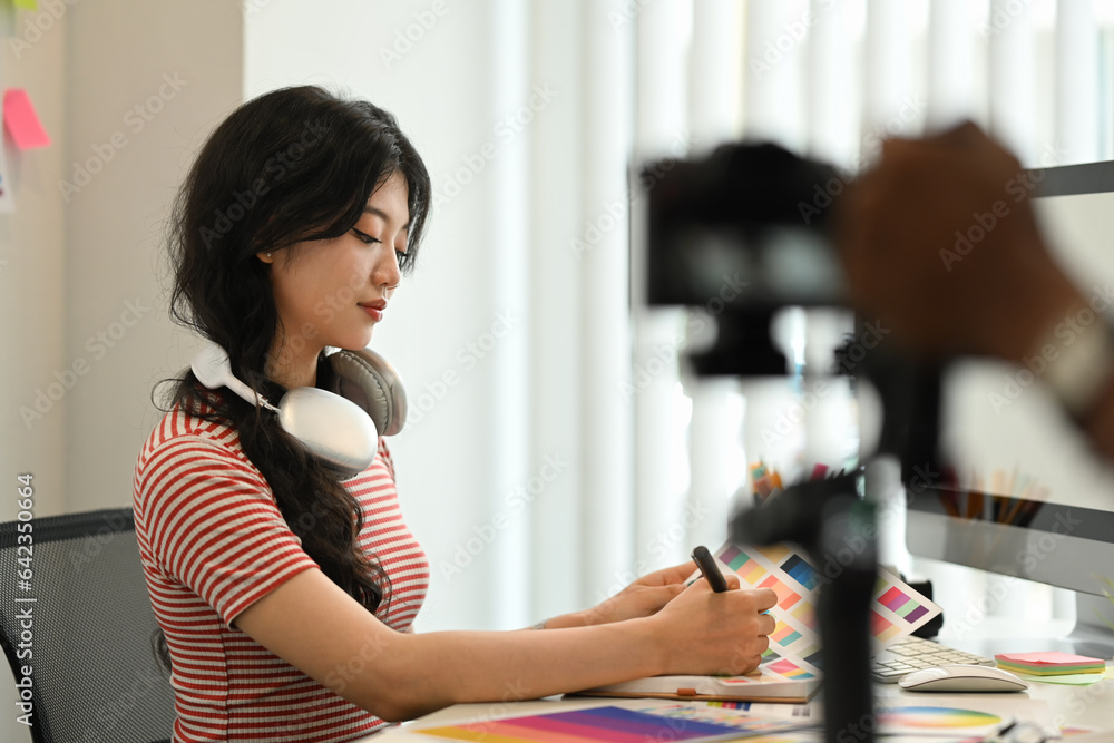 Asian woman female freelancer working on new design project and recording vlog on digital camera Asian woman female freelancer working on new design project and recording vlog on digital camera