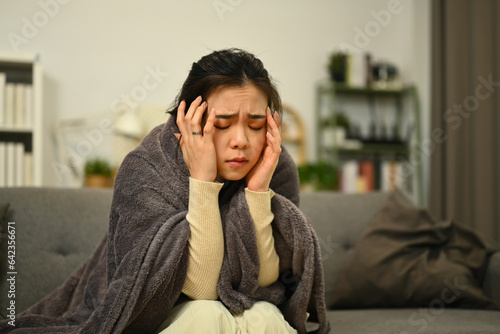 Ill upset young woman asian woman with with high fever and a flu sitting under the blanket. Health care concept