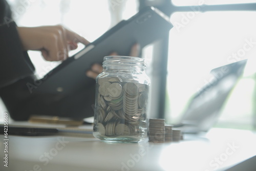 saving money and accounting concept. business man putting coin insert to jar and make acounting book for finance management to investment and saving. photo