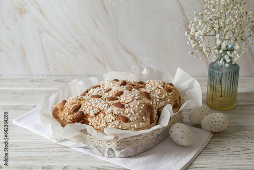 Delicious Italian Easter dove cake (traditional Colomba di Pasqua), decorated eggs and flowers on white wooden table. Space for text