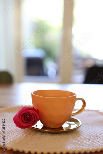 Cup of hot drink and red rose on table indoors