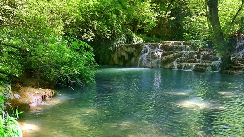 Waterfall and beautiful emerald stream in deep green forest.