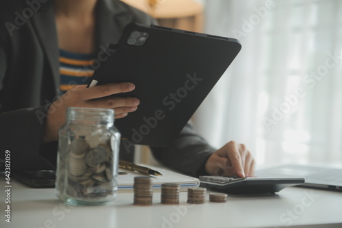 saving money and accounting concept. business man putting coin insert to jar and make acounting book for finance management to investment and saving. photo