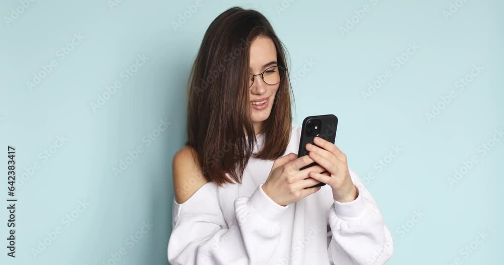 Happy satisfied girl is using her smartphone isolated on blue studio. Funny smiling girl is texting messages, flirting, coquette. Girl chatting with her boyfriend. Happy satisfied girl is using her smartphone isolated on blue studio. Funny smiling girl is texting messages, flirting, coquette. Girl chatting with her boyfriend.