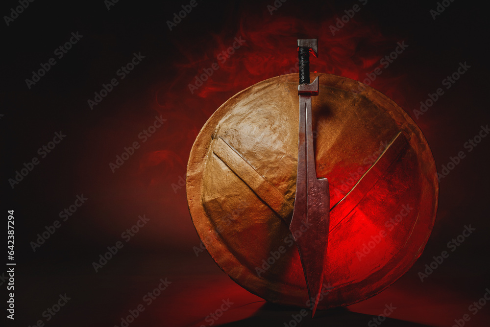 Ancient Spartan sword and shield on the dark background in the red light smoke concept. Spartan concept background with copy space.