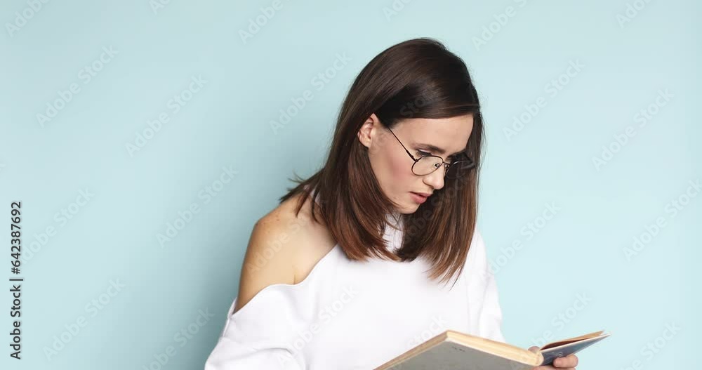 Close up view of calm caucasian attractive woman in eyeglasses reading book, turning page, learning, studying, education isolated on blue background. Close up view of calm caucasian attractive woman in eyeglasses reading book, turning page, learning, studying, education isolated on blue background.