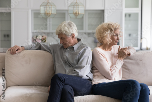 Silent ignoring older retired couple going through relationship problems, conflict, marriage crisis, sitting on home sofa back to back, keeping silence, thinking, looking away