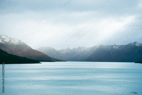 Snowy mountains near calm lake in cloudy day photo