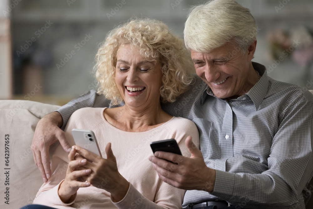 Happy older husband and wife holding smartphone, reading messages, playing online games, looking at screens, laughing, talking on video conference call, using app, enjoying Internet communication Happy older husband and wife holding smartphone, reading messages, playing online games, looking at screens, laughing, talking on video conference call, using app, enjoying Internet communication