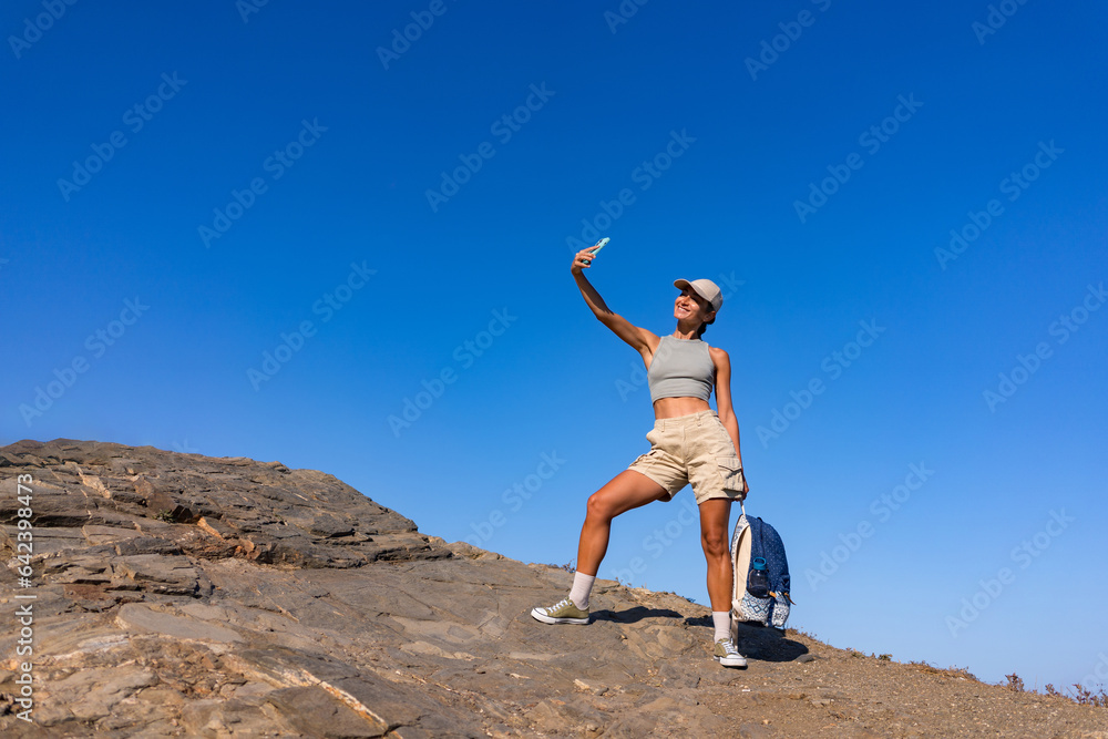 tourist girl with a backpack in the summer on top of a mountain takes a selfie against the backdrop of the sea and mountains tourist girl with a backpack in the summer on top of a mountain takes a selfie against the backdrop of the sea and mountains