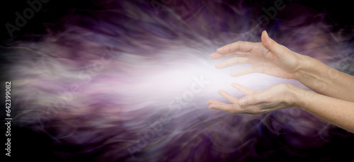 Beaming Reiki Healing Vibe Energy - Female parallel hands with bright white energy flowing outwards on a wide ethereal plum purple energy formation background and space for copy 