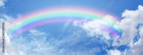 Stunning wide blue sky and bright rainbow - big fluffy clouds with a giant arcing rainbow against a beautiful summer time blue sky with copy space for positive spiritual messages 