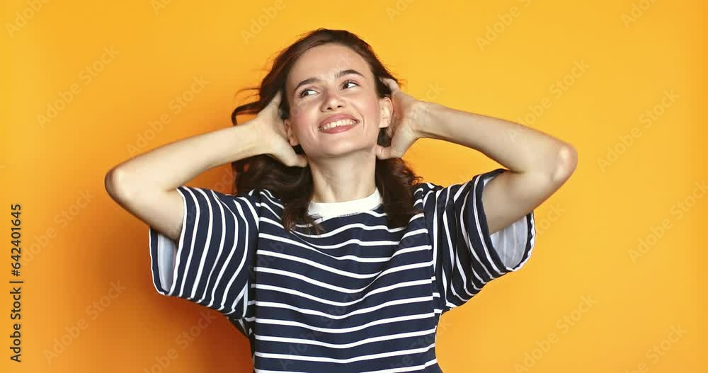 Lovely coquettish brunette woman, winking playfully, flirting. Woman fix her hair isolated on yellow background. Curly hair fashion model face smiling. Girl look at camera. Lovely coquettish brunette woman, winking playfully, flirting. Woman fix her hair isolated on yellow background. Curly hair fashion model face smiling. Girl look at camera.