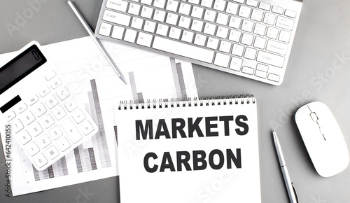 MARKETS CARBON text written on notebook on grey background with chart and keyboard, business concept