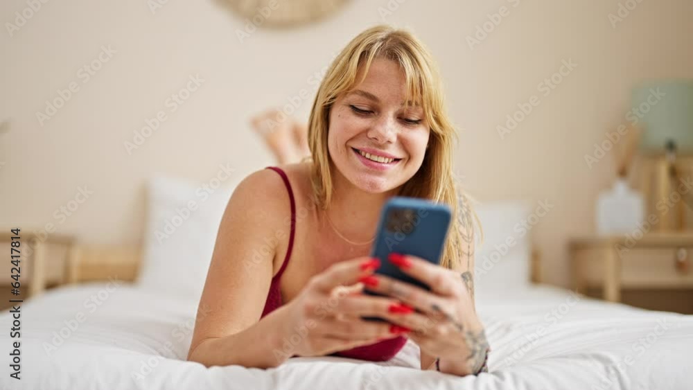 Young blonde woman wearing sensual lingerie lying on bed using smartphone at bedroom Young blonde woman wearing sensual lingerie lying on bed using smartphone at bedroom