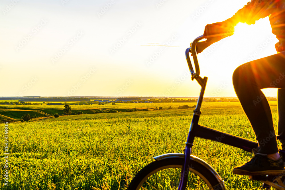 Naklejka premium woman riding a bike through a field at sunset.