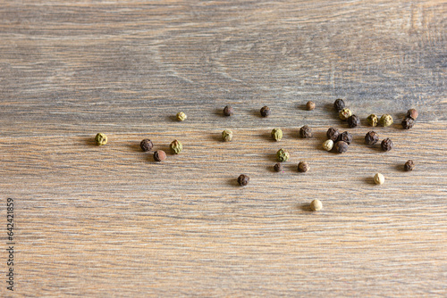 Peas of multi-colored pepper are scattered on a wooden table.