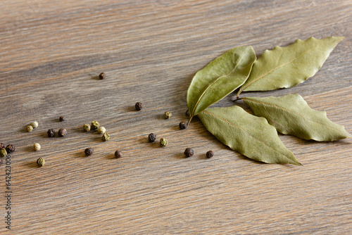 Peppercorns and bay leaves are scattered on a wooden table.