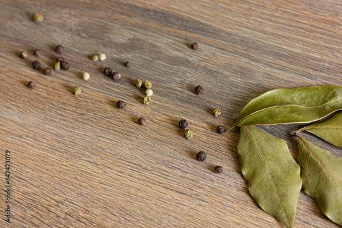 Peppercorns and bay leaves are scattered on a wooden table.