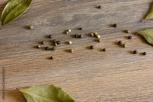 Peppercorns and bay leaves are scattered on a wooden table.