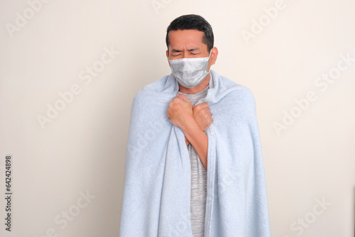 A man wearing medical mask and covering his body with blanket when got fever photo