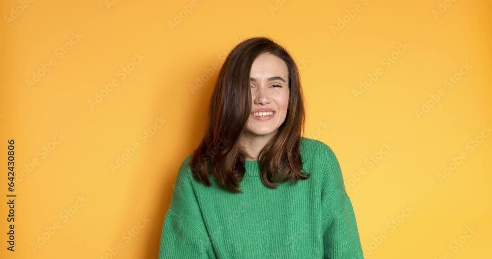 Friendly girl makes hello gesture glad to meet friend. Hi nice to meet you. Brunette girl wear green sweater wave hand isolated on yellow background Friendly girl makes hello gesture glad to meet friend. Hi nice to meet you. Brunette girl wear green sweater wave hand isolated on yellow background