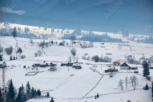 Winter landscape with small village houses between snow covered forest in cold mountains