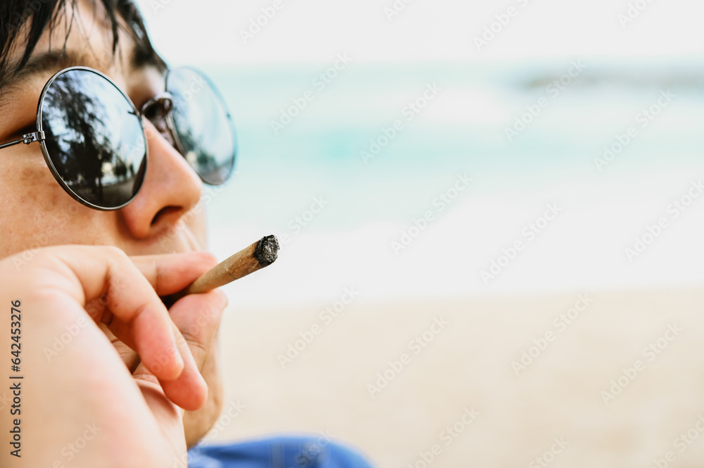 Young man smoking drug medical cannabis, weed at the beach.