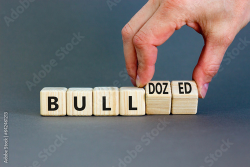 Bull or bulldozed symbol. Businessman turns wooden cubes and changes word Bull to Bulldozed. Beautiful grey table grey background. Business bull or bulldozed concept. Copy space.