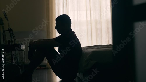 Silhouette of depressed man sitting on a floor. Sad unhappy person in a bedroom thinking about something photo