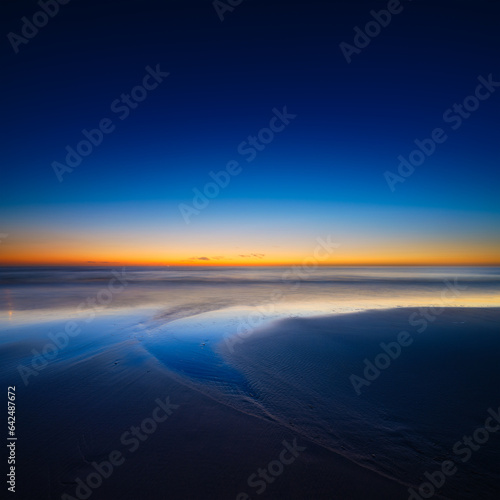 A seascape during sunset. Lines of sand on the seashore. Bright sky during sunset. A sandy beach at low tide. Wallpaper and background. © biletskiyevgeniy.com