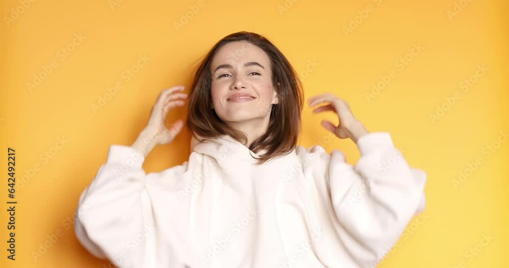 Stylish girl. Beautiful model close up portrait. Sensual brunette putting hood on head. Young woman in white hoodie on yellow background. Concept of comfort and soft clothes. Stylish girl. Beautiful model close up portrait. Sensual brunette putting hood on head. Young woman in white hoodie on yellow background. Concept of comfort and soft clothes.