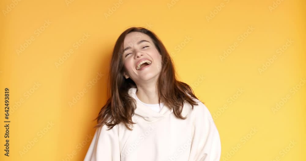 Friendly looking positive straight hair woman shows shaka sign gestures, tongue out indoor being in high spirit, wears white hoody isolated on yellow background. Hang loose! Friendly looking positive straight hair woman shows shaka sign gestures, tongue out indoor being in high spirit, wears white hoody isolated on yellow background. Hang loose!