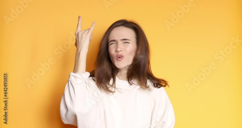 Carefree delighted beautiful girl scream woo and rock and roll hand gesture, punk sign, shouting excited by win. indoor studio shot isolated on yellow background