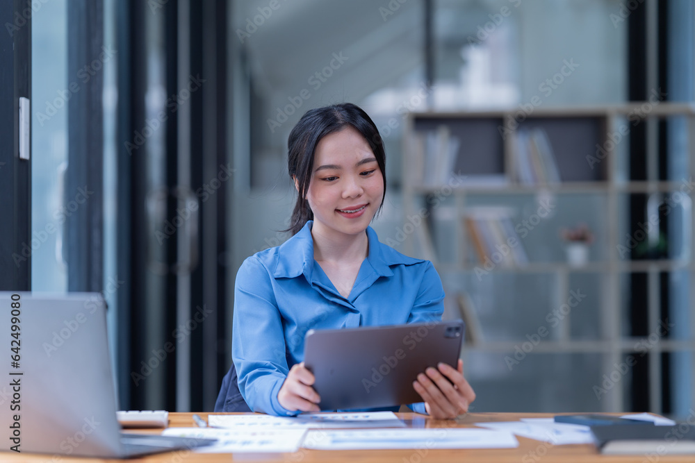 Smiling female browsing laptop and tablet sitting at table with papers and books while in the office. Smiling female browsing laptop and tablet sitting at table with papers and books while in the office.