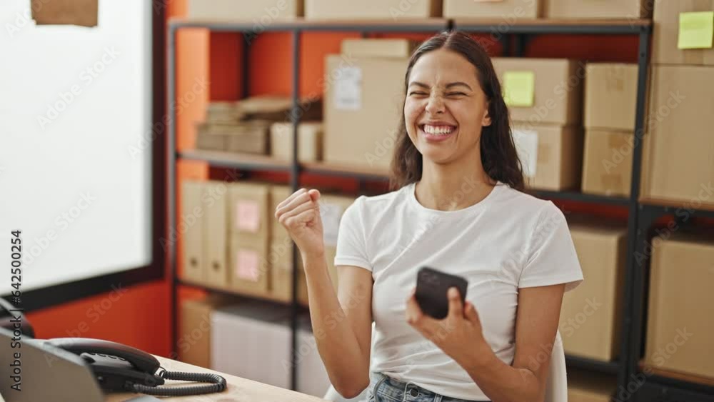 African american woman ecommerce business worker using smartphone celebrating at office African american woman ecommerce business worker using smartphone celebrating at office