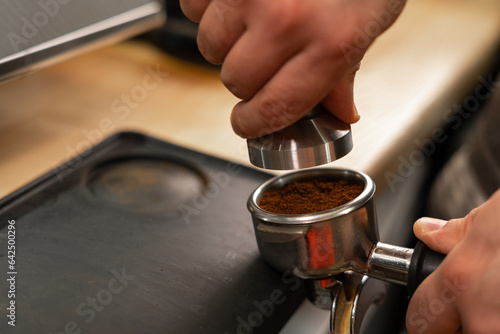 Barista holding portafilter and coffee tamper making an espresso in cafe, close-up.