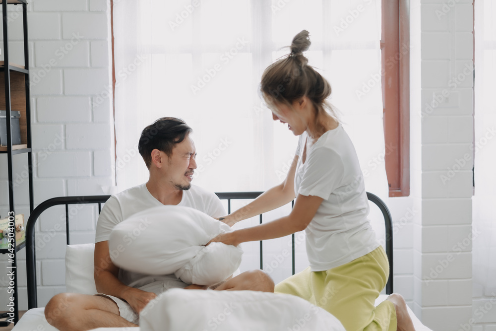 Asian wife and husband playing pillow fight funny and laugh on the bed.