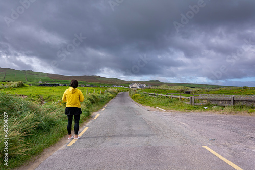 Lonely person with yellow jacket standing on the road through green fields on a cloudy stormy day