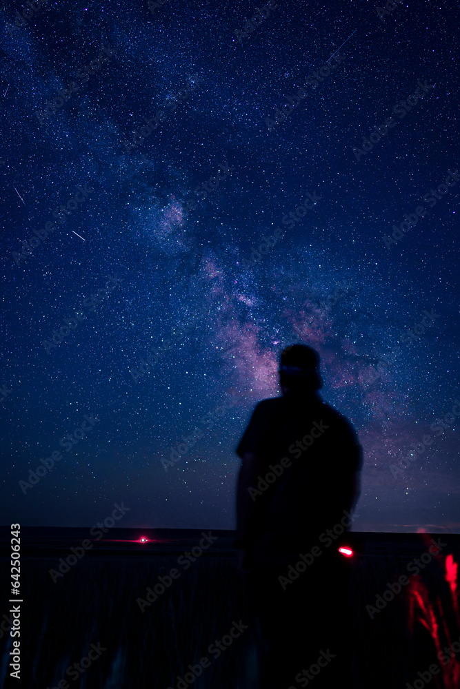 Milky Way with silhouette of man standing in foreground under galaxy center stars in pink and blue dark sky wyoming astrophotography astro space science
