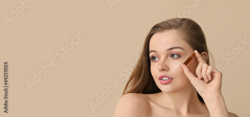 Beautiful young woman holding ampule on beige background with space for text. Skin care concept