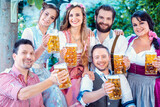 Group of merry people drinking beer holding the glasses into the camera