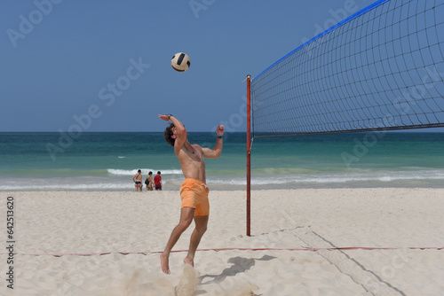 Volleyball player hitting the ball over the net on the beach