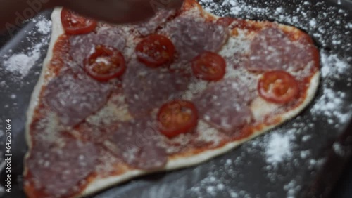 Adding sliced cherry tomatoes to heart shaped pizza on the baking tray. Preparing heart shaped pizza for Valentine's Day for a loved one. 4K video. Artistric shooting photo