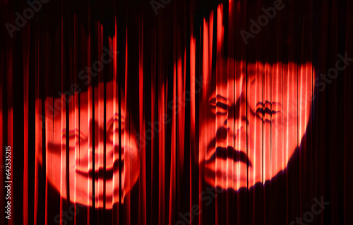 Two theatre masks, one smiling and one frowning, projected on a red curtain. One representing comedy and the other representing tragedy. The curtain is made of red velvet