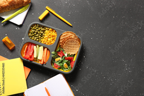 Lunchbox with delicious food and different stationery on grunge black background photo