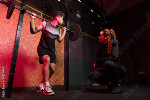 Personal trainer instructing student in barbell squats at gym