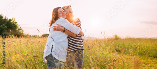 Portrait of sincerely smiling young pregnant woman dressed in light summer clothes with mother in evening sunset hours. They are hugging tight. Woman's health, human in the nature concept image.
