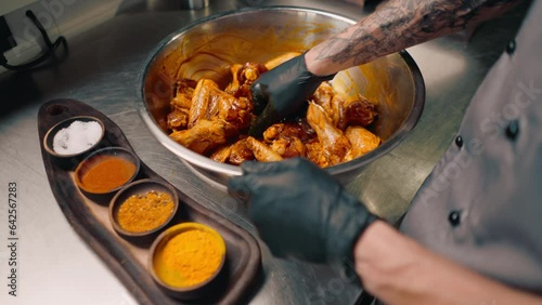 professional restaurant kitchen chef stirs chicken wings with spices in a bowl asian dish close-up