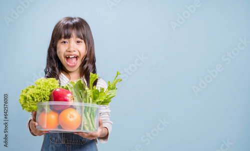 A little girl is holding a bowl with mixed vegetables and fruits.